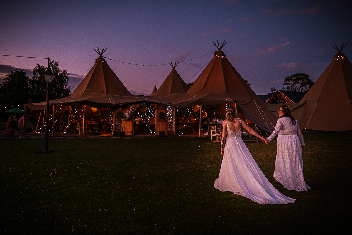 Two Brides Holding Hands Walking Towards Tipi at Bridge House Barn Wedding