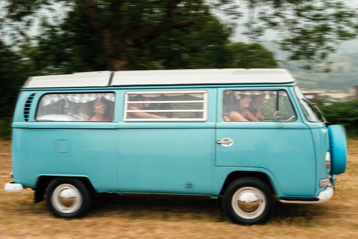 Grainy, blurry artistic photo of a VW campervan arriving at Derbyshire festival wedding with bridesmaids and bride on board.